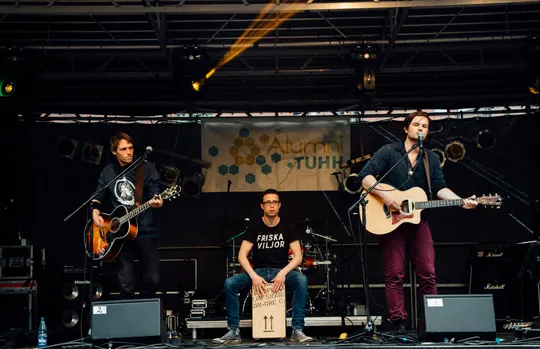 Falke Collective mit zwei Akustikgitarren und Cajón auf einer überdachten Außenbühne.