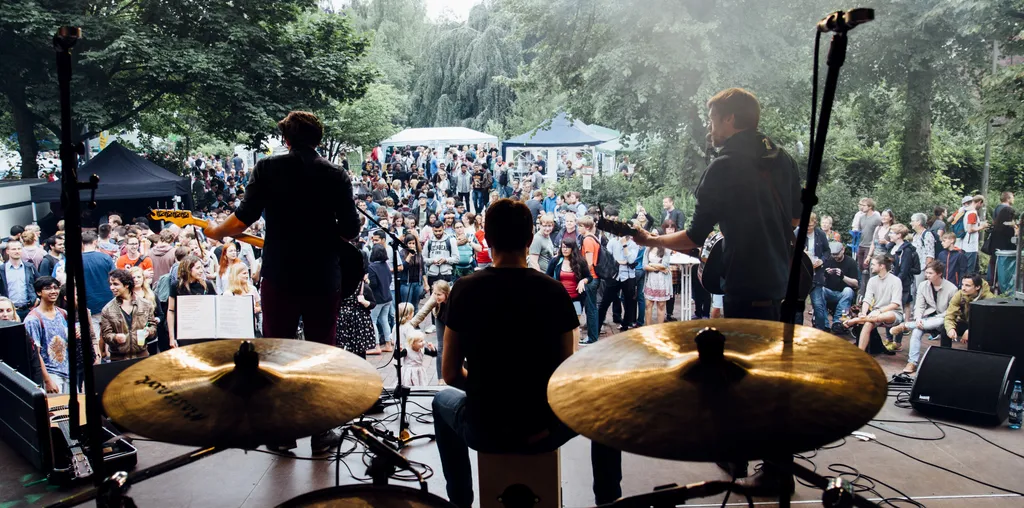 Blick von hinter dem Schlagzeug über die Band auf das Publikum im Freien.